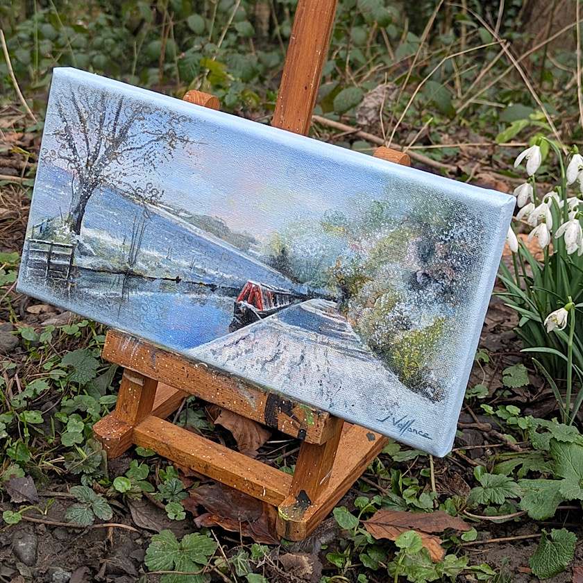 side view of small painting of red narrowboat in snow on an easel.