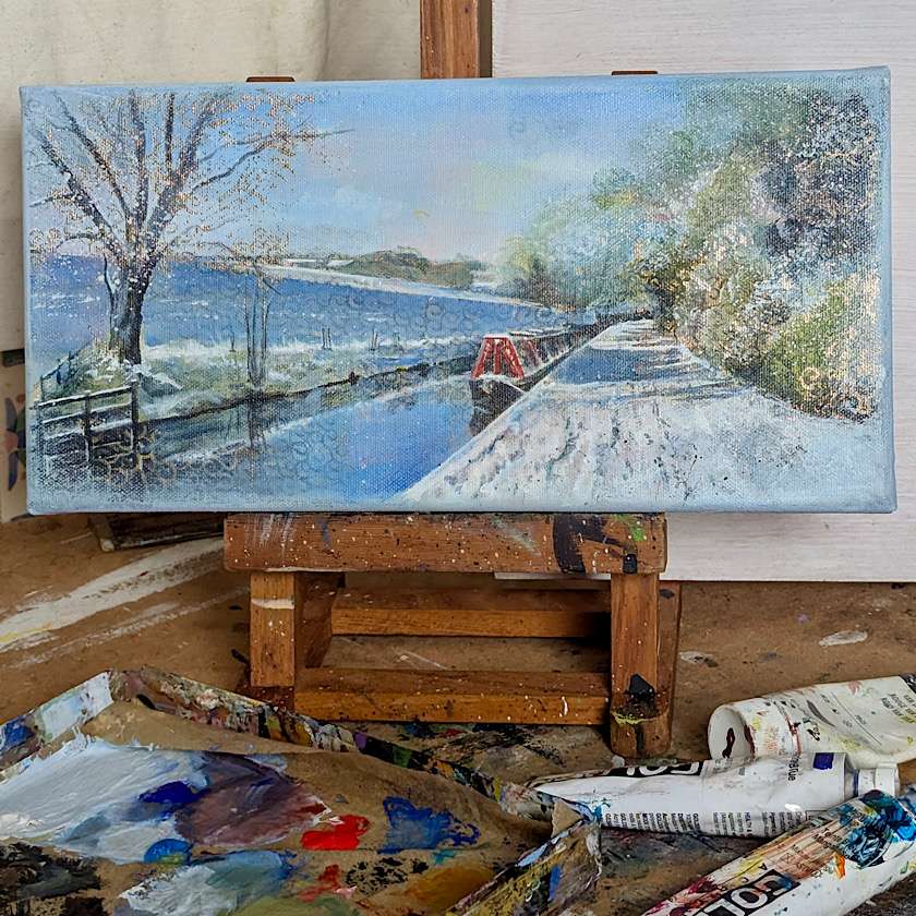 landscape painting of red boat in snow on easel with messy table